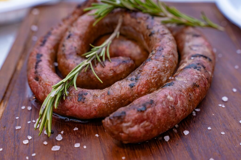 Close-up of a grilled sausage garnished with rosemary, capturing rustic flavors on a wooden board.